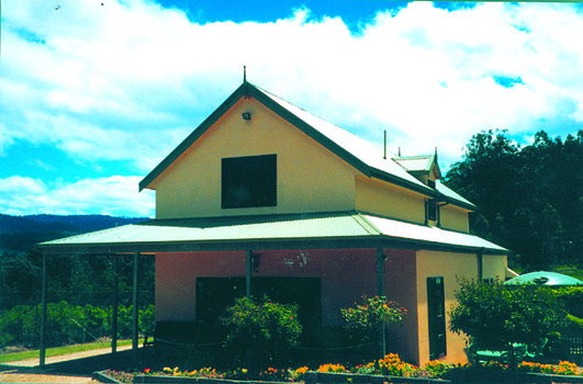 Shows a rendered two storey building surrounded by gardens. There is a verandah running along the front and left side of the building.