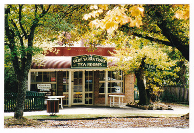 Shows the front facade of the Olde Yarra Track Tea Rooms in Marysville in Victoria. Shows two tables located out the front of the rooms under the bull nosed verandah.