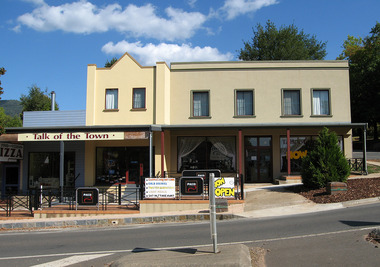 Shows the Talk of the Town shop in Marysville in Victoria. Shows a double storey building with a verandah at the front. There is a sign across the front of the verandah with the name of the shop. There are signs advertising pizza, various beverages and other meals that are available.