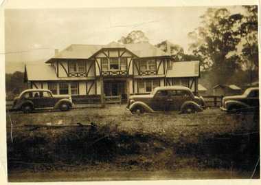 Shows Misty Hills Guest House in Narbethong in Victoria. Shows a large tudor style building. There are three cars parked in front of the building.