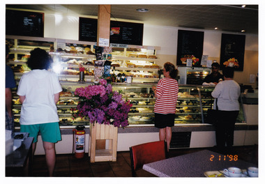 Shows the interior of the Marysville Country Bakery in Victoria. Shows customers standing in front of the glass fronted counters which are filled with baked products for sale. 