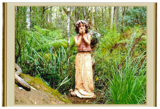 Shows a terracotta sculpture of a young girl standing with a duck at her feet. The girl is wearing a vest like top and a long skirt and has shoulder length hair. She is holding her hands to her mouth.