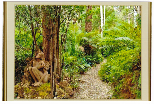 Shows a terracotta sculpture of a naked woman with long hair sitting against a tree. She has her knees drawn up to her body and is holding something in her right hand against her left arm. She is looking up at something above her.