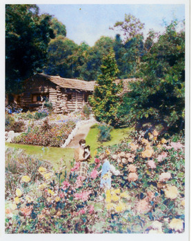 Shows The Log Cabin in Marysville in Victoria. Shows the extensive gardens in the grounds of The Log Cabin. Shows a lady holding a black cat with a young girl who is standing in a flower bed.