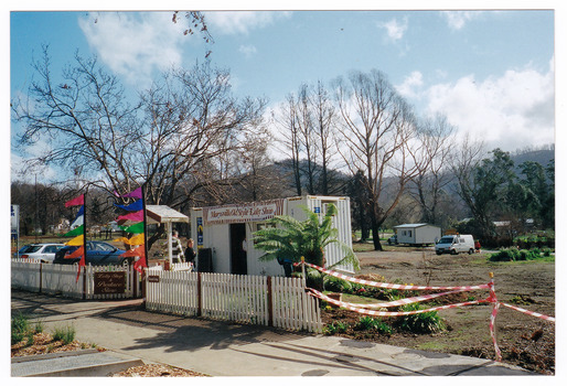 Shows the temporary premises of the Marysville Old Style Lolly Shop in Victoria. Shows a shipping container which is situated behind an old picket fence and is surrounded by bare earth.