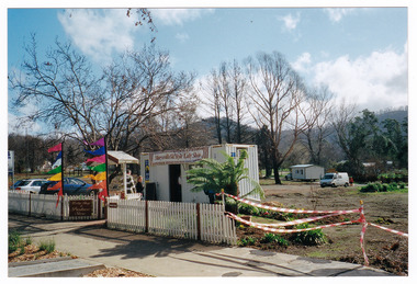 Shows the temporary premises of the Marysville Old Style Lolly Shop in Victoria. Shows a shipping container which is situated behind an old picket fence and is surrounded by bare earth.