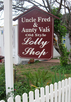 Shows the sign and the fence in front of Uncle Fred & Aunty Val's Old Style Lolly Shop in Marysville in Victoria. In the background can be seen the shipping container that became the Lolly Shop's temporary premises after the original building was destroyed in the 2009 Black Saturday bushfires.