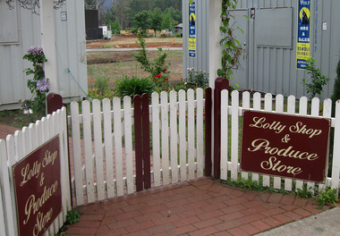 Shows the signs and the fence in front of Uncle Fred & Aunty Val's Old Style Lolly Shop in Marysville in Victoria. In the background can be seen the shipping container that became the Lolly Shop's temporary premises after the original building was destroyed in the 2009 Black Saturday bushfires.