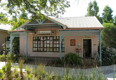 Shows the front facade of Marysville Country Real Estate in Victoria. Shows a weatherboard building fronted by a verandah. In the windows are display several notices of properties for sale.