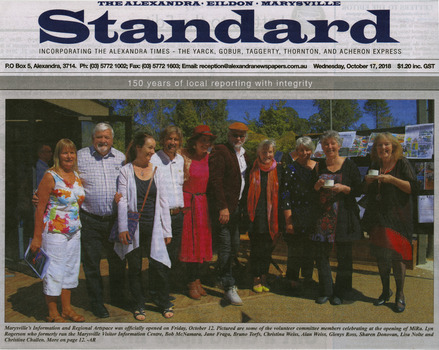 Shows a newspaper photograph of a group of ten people standing in front of the building that houses MiRa.