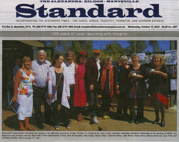 Shows a newspaper photograph of a group of ten people standing in front of the building that houses MiRa.