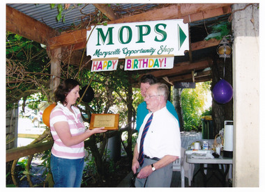 Shows a colour photograph of a plaque being presented to volunteers at MOPS-Marysville Opportunity Shop.
