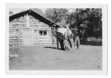 Shows The Log Cabin in Marysville in Victoria. Shows a group of four with a horse. There is a young person sitting on the horse with a man holding the reins. There are two girls standing in front of the horse. All are wearing jodphurs.