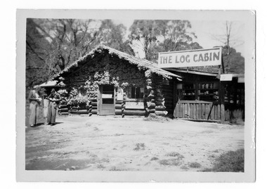 Shows The Log Cabin in Marysville in Victoria. Shows the front facade with two people standing out the front of the building.