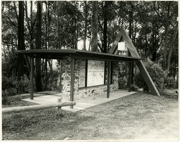 Shows the tourist information board that is at the entrance to Marysville. Shows a structure constructed of rocks and timber. There are information boards of local attractions along with two maps; one of the township and one of the local area. At one end of the building is a large wooden triangle which represents 'The Triangle' of which Marysville is included.