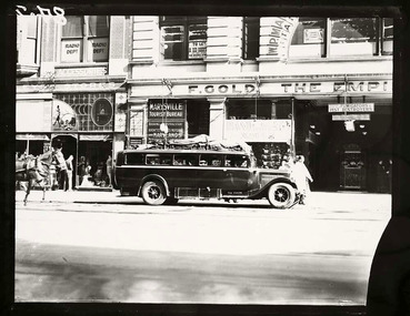 Shows a black and white photograph of the Marysville Tourist Bureau in Melbourne. Shows the building with a the bus waiting out the front to take passengers from Melbourne to Marysville.