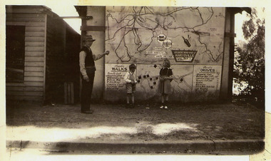 Shows a man, a young boy and girl standing in front of a large map which has been adhered to the outside wall of a building. The map is of the area surrounding Marysville. There is also a list of popular walks in the area as well as a list of popular drives throughout the district.