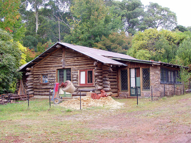 Shows The Log Cabin in Marysville in Victoria. Shows a cement mixer next to a small pile of sand and some red bricks.