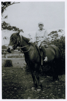 Shows a member of the Branchflower family in Marysville in Victoria. Shows a woman sitting astride a saddled horse.