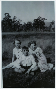 Shows members of the Branchflower Family in Marysville in Victoria. Shows a women, a young girl and a boy sitting in a paddock with a background of forest.