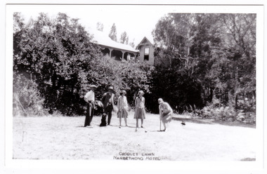 Shows a group of two men and three women playing croquet on the lawn in front of the Narbethong Hotel.
