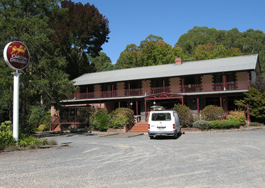 Shows a colour photograph of the Black Spur Inn in Narbethong. Shows a large double storey building with a verandah running along the front of both floors. Shows a van parked at the front entrance stairs. Shows an advertising sign for Carlton Draught beer.