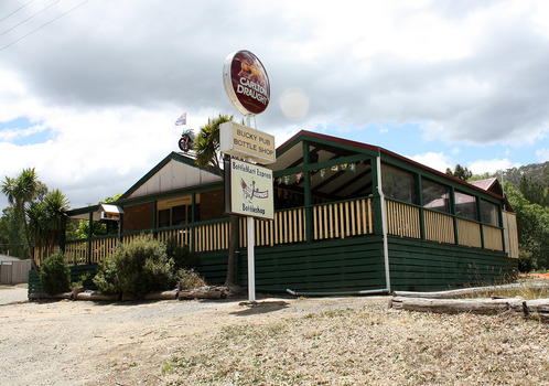 A colour photograph of the Buxton Hotel in Buxton. Shows a large building with a verandah surrounding it. Shows a sign located out the front of the building advertising Carlton Draught and the Bucky Pub bottle shop as part of the BottleMart Express bottleshops.