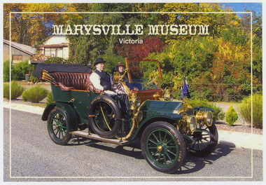 Shows a green vintage car. Aboard are a man, who is driving and a lady passenger. Both are in costume. 