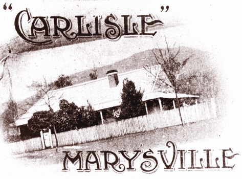 A copy of an old black and white photograph of Carlisle Guesthouse in Marysville. Shows an old weatherboard building with a verandah running all the way around. Shows a wooden picket fence running along the front of the property.