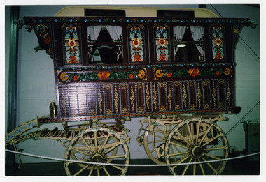 Shows the side view of the Romany Vardo Gypsy wagon that was housed in The Marysville Museum in Marysville in Victoria. Shows the ornately painted window surrounds and the painted and decorated wheels.