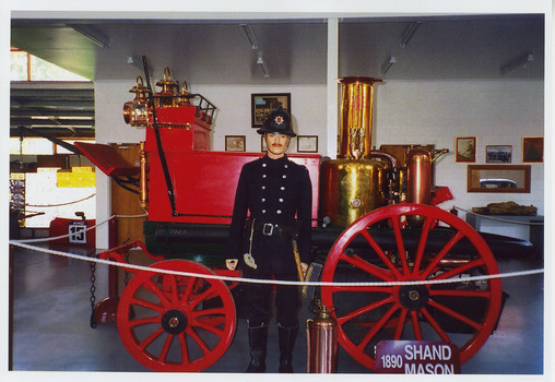 Shows a 1890 Shand Mason horse-drawn fire engine that was housed in The Marysville Museum in Marysville in Victoria. Shows a male mannequin dressed in a fireman's uniform standing next to the fire engine. Also shows an old fire extinguisher made of copper.