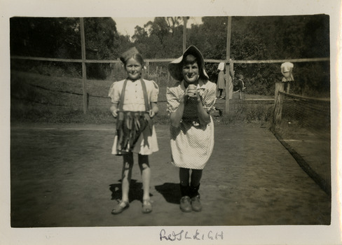 A black and white photograph of two unknown children wearing dress ups whilst standing on the tennis court at Roseleigh in Marysville. The photograph was taken in 1954.