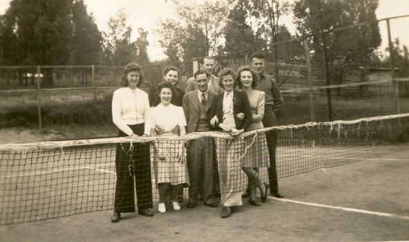 A digital copy of a black and white photograph of Pat and Ewen Cumming with a group of unknown people standing on the tennis court at Roseleigh. The photograph shows Pat Cumming 3rd from the left and Ewen Cumming at the far right of the group. The original photograph was taken in 1945.