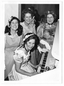 A black and white photograph of three local ladies sitting and standing at the piano in The Marysville Hotel in Marysville. The photograph was taken in 1969.