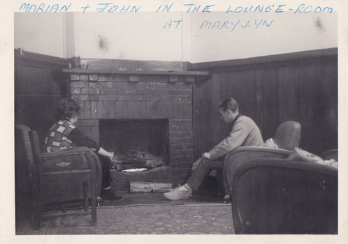 A black and white photograph taken at Mary-Lyn Guest House in Marysville. Mary-Lyn was a part of the Mary Chain of guest houses built by Eric Dowdle in the Depression years. The photograph is of the two guests seated in the lounge room in Mary-Lyn.