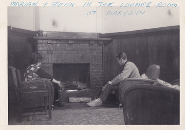 A black and white photograph taken at Mary-Lyn Guest House in Marysville. Mary-Lyn was a part of the Mary Chain of guest houses built by Eric Dowdle in the Depression years. The photograph is of the two guests seated in the lounge room in Mary-Lyn.