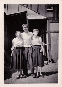 A black and white photograph taken at Mary-Lyn Guest House in Marysville. Mary-Lyn was a part of the Mary Chain of guest houses built by Eric Dowdle in the Depression years. The photograph is of two ladies and a young man standing outside the main building at Mary-Lyn.