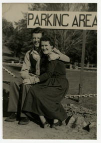 A black and white photograph taken at Mary-Lyn Guest House in Marysville. Mary-Lyn was a part of the Mary Chain of guest houses built by Eric Dowdle in the Depression years. The photograph was taken in 1954 and is of Warren Titcher and Marg Martin sitting in the car park at Mary-Lyn.