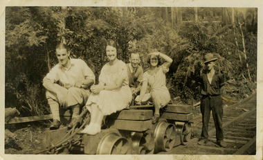 A black and white photograph of a group of guests who were staying at Mary-Lyn Guest House in Marysville. Mary-Lyn was a part of the Mary Chain of guest houses built by Eric Dowdle in the Depression years. The photograph, which was taken in 1933, shows a group of men and women sitting on top of a timber tramway logging jinker.