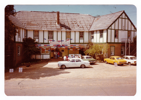 A colour photograph taken at Mary-Lyn Guest House in Marysville. Mary-Lyn was a part of the Mary Chain of guest houses built by Eric Dowdle in the Depression years. The photograph shows a view of the rear entrance of the main building with a banner above the door that says "Sterlings Tavern".