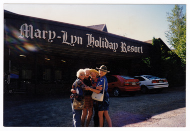 A colour photograph taken at Mary-Lyn Holiday Resort in Marysville. Mary-Lyn was a part of the Mary Chain of guest houses built by Eric Dowdle during the Depression years. The photograph shows a group of four unknown people standing outside the front of the resort.