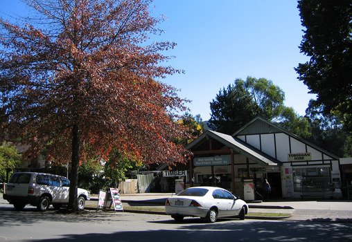 Shows the front facade of the Marysville Auto and Hardware Centre in Marysville in Victoria. Shows the front of the building with two petrol bowsers out the front. Shows a sign advertising toboggan hire.