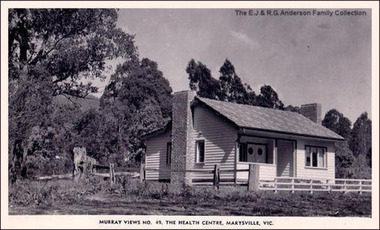 Shows a weatherboard building surrounded by a wooden rail fence. At the side of the building is a large brick chimney.