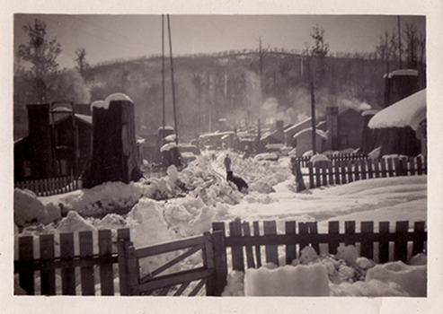 A black and white photograph of Cambarville township during winter. Cambarville was established as a timber mill town in the 1940s. Timber mill owners A. Cameron and F.J. Barton named Cambarville. They established the mill to salvage timber from trees destroyed in the 1939 bushfires. Cambarville was impacted by the 2009 Black Saturday bushfires and any remaining structures were destroyed. The photograph was taken in 1955.