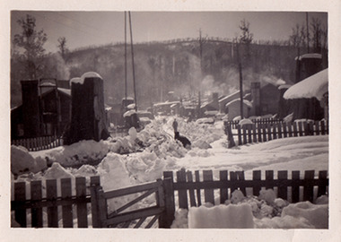 A black and white photograph of Cambarville township during winter. Cambarville was established as a timber mill town in the 1940s. Timber mill owners A. Cameron and F.J. Barton named Cambarville. They established the mill to salvage timber from trees destroyed in the 1939 bushfires. Cambarville was impacted by the 2009 Black Saturday bushfires and any remaining structures were destroyed. The photograph was taken in 1955.