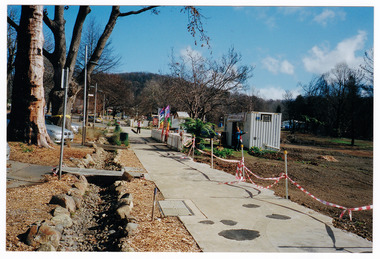 Shows the temporary premises of the Marysville Old Style Lolly Shop in Victoria. Shows a shipping container which is situated behind an old picket fence and is surrounded by bare earth.
