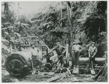 A copy of a black and white photograph of a group of men standing with a donkey engine and winching gear used to haul logs from the forest.