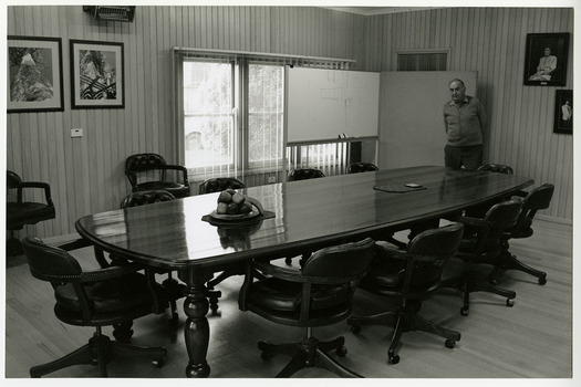 A black and white photograph of Lloyd Gould standing in the boardroom of J.L. Gould Sawmills Pty. Ltd.