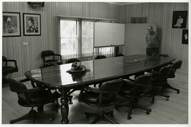 A black and white photograph of Lloyd Gould standing in the boardroom of J.L. Gould Sawmills Pty. Ltd.