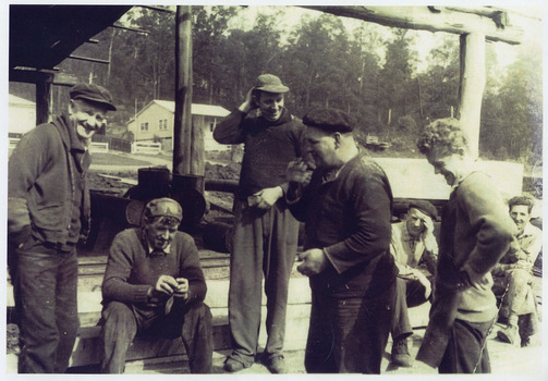 A copy of a black and white photograph taken at 'smoko' at Goulds Sawmill in Marysville. The original photograph was taken in 1950-1960 and shows a group of men standing around enjoying their smoko break.